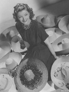 a woman sitting on the ground with many hats around her and smiling at the camera