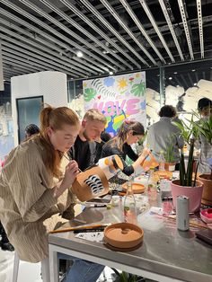 a group of people sitting around a table working on crafting projects with plants in the background