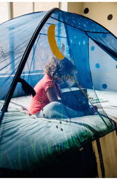 a woman sitting on top of a bed next to a blue tent with a banana