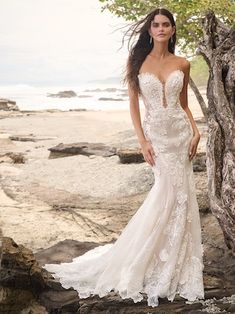 a woman in a wedding dress standing on rocks near the ocean