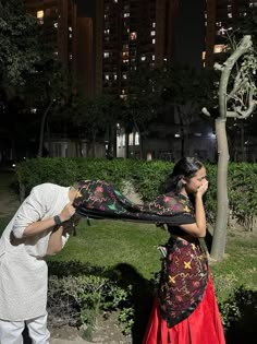 a man and woman standing next to each other in front of a tree at night