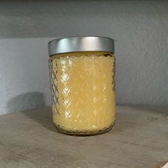 a yellow candle sitting on top of a wooden table next to a metal container filled with liquid