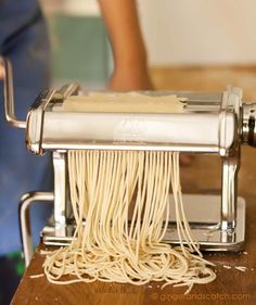 a close up of a pasta maker on a wooden table with someone in the background