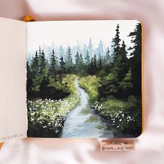 an open book with a painting of a path in the woods