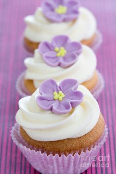 three cupcakes with white frosting and purple flowers