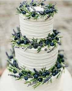 a three tiered white cake with blue berries and greenery