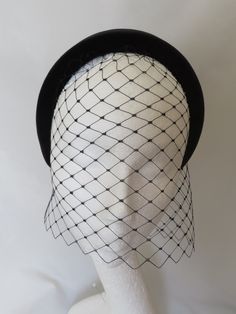 a white mannequin head wearing a black hat with netting on it's brim