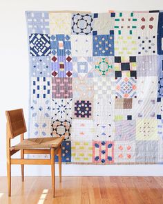 a wooden chair sitting in front of a large quilt on the wall next to a chair