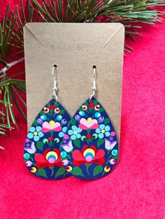 a pair of earrings with flowers painted on them sitting next to a christmas tree branch