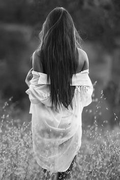 a woman walking through tall grass with her back turned to the camera and long hair blowing in the wind