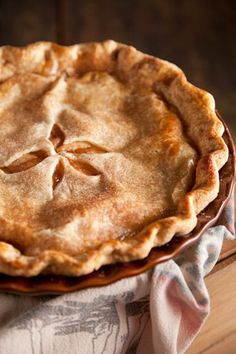 a pie sitting on top of a wooden table next to a white and blue towel