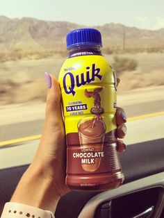 a woman holding up a bottle of chocolate milk in her hand while driving down the road