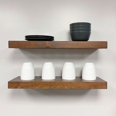 three wooden shelves with white cups and plates on them, one black bowl is sitting on top of the shelf