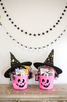 two pink buckets filled with halloween treats on top of a wooden table in front of a white wall