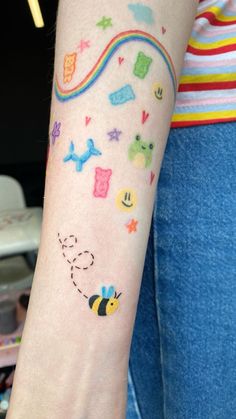 a woman's arm with tattoos on it, including a bee and rainbows