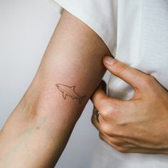 a woman's arm with a small tattoo of a shark on her left arm