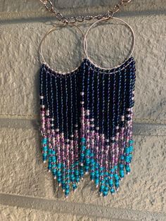 two hoop earrings with blue and purple beads hanging from a chain on a brick wall