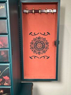 an orange wall hanging on the side of a blue cabinet next to drawers with flowers painted on it