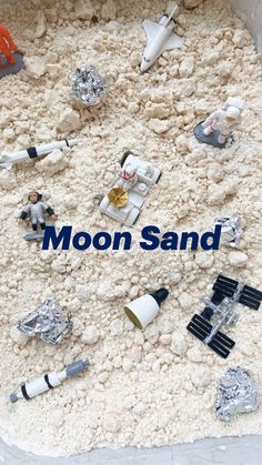 an assortment of toy space related items are in a plastic container filled with white sand