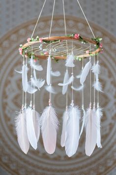 a white dream catcher with feathers hanging from it's sides and flowers on the side