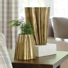 two gold vases sitting on top of a wooden table next to a white block