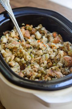 a crock pot filled with stuffing and carrots next to a fork in it