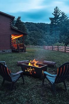 a fire pit with chairs around it in the grass near a barn and trees at night