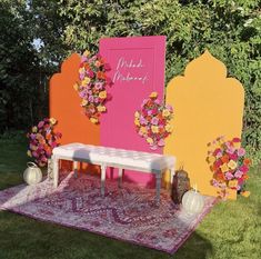 a pink and yellow wedding backdrop with flowers on the bench, in front of an arch