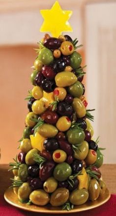 a christmas tree made out of olives and other fruits on a table with plates