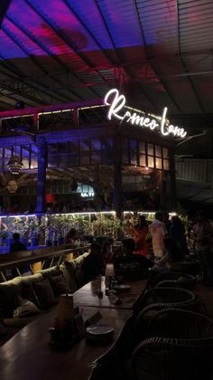 people sitting at tables in front of a bar with neon lights on the ceiling and windows