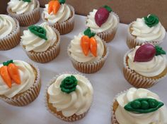 twelve cupcakes with white frosting and carrots on top are arranged in a box