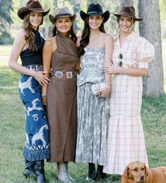 three women and a dog are posing for a photo in front of a large tree