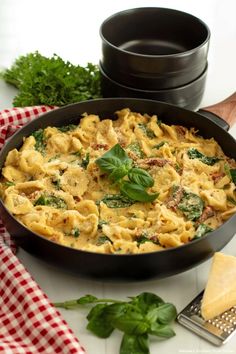 a skillet filled with pasta and spinach on top of a table next to cheese