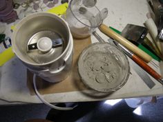 a table topped with lots of different types of art supplies next to a cup filled with paint