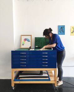 a woman standing next to a blue drawer on top of a wooden table with drawers