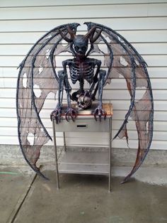 a skeleton sitting on top of a table in front of a white building with an open door