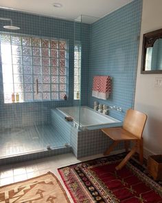 a blue tiled bathroom with a bathtub, rug and chair in front of it