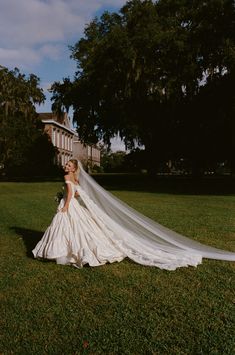 a woman in a wedding dress is standing on the grass with her long veil flowing