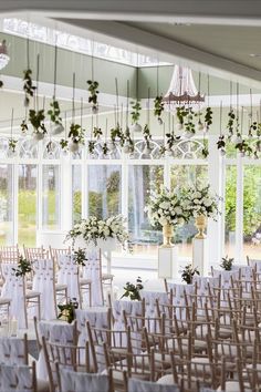 rows of chairs with white sashers and flowers in vases hanging from the ceiling