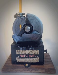 an old fashioned machine is sitting on top of a wooden block with a yellow handle