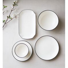 four white plates with black rims are arranged on a gray surface next to a flower