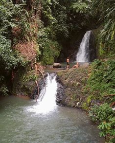 two people standing at the base of a waterfall