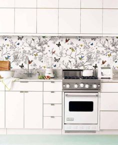 a kitchen with white cabinets and a silver stove top oven in front of a wallpapered backsplash