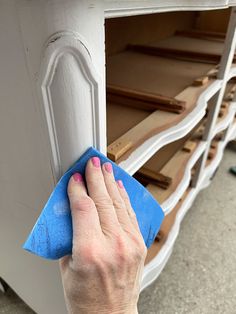 a person with a blue cloth on their hand wiping up the paint off an old dresser