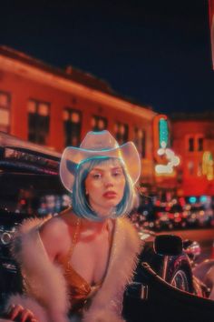 a woman with blue hair wearing a cowboy hat and fur coat sitting in a car