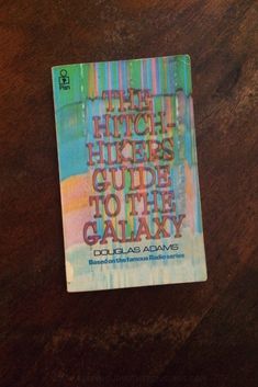 the hitchhikers guide to the galaxy book sitting on a wooden table next to a cell phone