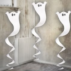 three white paper hangings in the shape of ghost faces on a wall next to a radiator