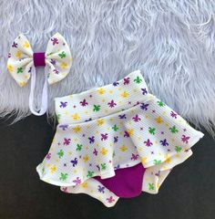 "Just in time for all of the Mardi Gras celebrations is this purple, green and gold (yellow) \"Fleur De Lis Skirted Bummie and Bow Set. It's unique in every way and great for parades, parties, family gatherings, photo shoots or a fun dress up day. They are made with super soft, stretchy and comfortable, breathable knit for hour long Mardi Gras fun. The design may vary slightly due to the availability of the fabric from our supplier but it shouldn't change the over all look of the item. Custom orders are welcomed. Should you need your order sooner than 7-14 business days just message me. Please make note at checkout as to the date you need your order so that the date won't be over looked. Some of our items have small parts so adult supervision is recommended." Cute Fitted Bottoms With Built-in Shorts, Fitted Bottoms With Built-in Shorts In Cute Style, Cute Purple Cotton Bottoms, Cute Fitted Purple Bottoms, Cute Purple Shorts For Spring, Purple Cotton Skort For Summer, Summer Purple Cotton Skort, Fitted Purple Skort With Built-in Shorts, Playful Fitted Purple Bottoms