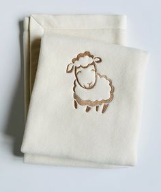 two napkins with embroidered sheep on them, one white and the other gold colored