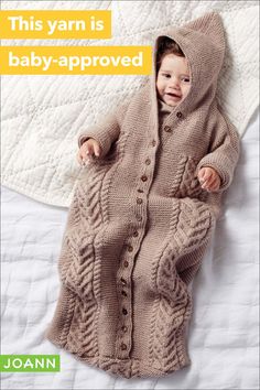 a baby in a knitted cardigan laying on a bed